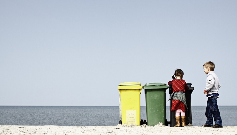 Kinder vor farbigen Mülltonnen am Strand